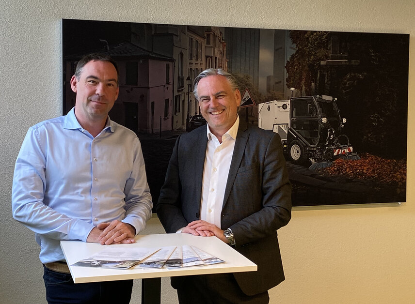 Henning Schröder (l.) und Gerhard Neudorfer am Hauptsitz der Aebi Schmidt Group vor dem Bild einer Schmidt Flexigo, die heute das kann, was wir auch bei den Grossgeräten in Zukunft mehr sehen werden.